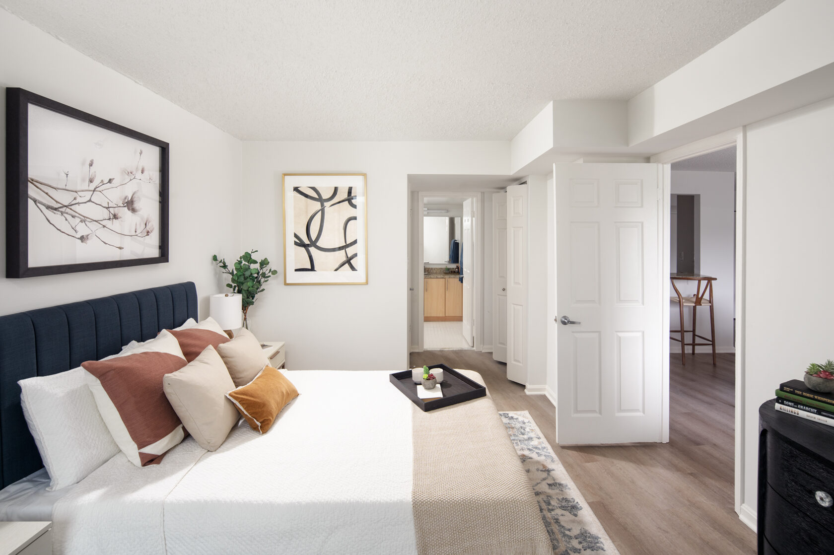 A side view of a contemporary bedroom with warm wood flooring and doors opening onto a walk-in closet and master bathroom.